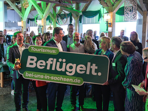 Vertreter aus der Politik, darunter auch Landrat Thomas Hennig, halten ein grünes Schild, auf dem steht: Tourismus Beflügelt. 